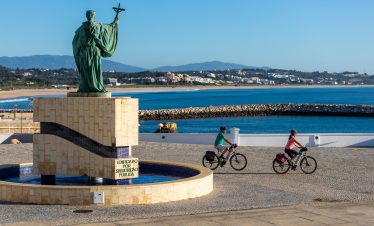 Cyclists riding past statue by the sea in Portugal
