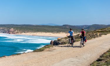 Two cyclists riding along dirt path by the Atlantic Ocean