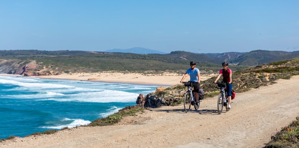 Two cyclists riding along dirt path by the Atlantic Ocean