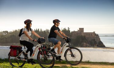 Riders passing monument with ocean backdrop