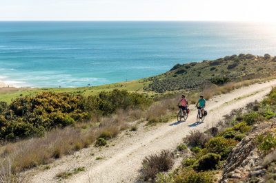 Two cyclists riding on gravel road by Algarve coast